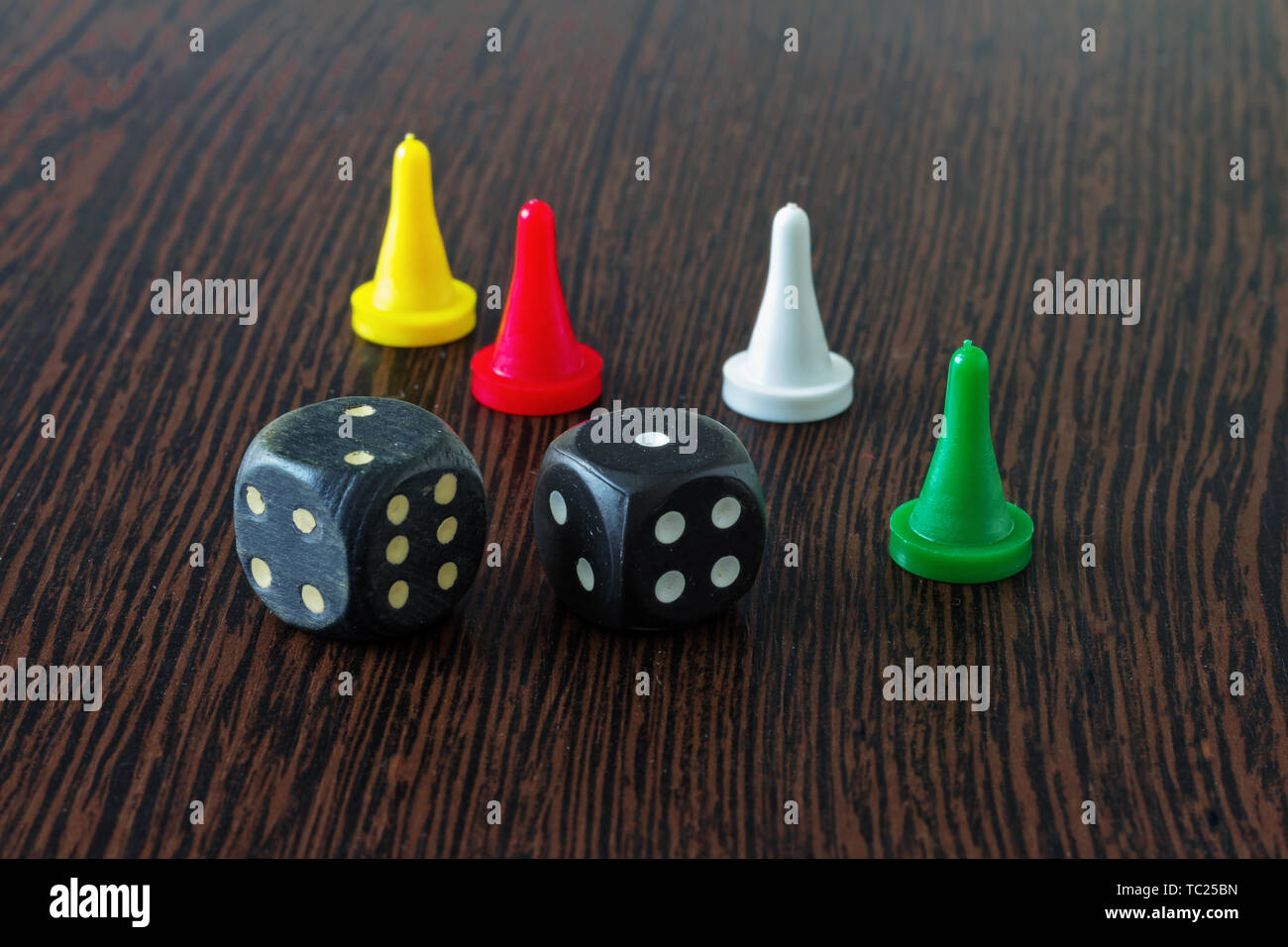 Quatre jetons de couleurs différentes et deux dés pour jeux de société sur une surface en bois. Banque D'Images
