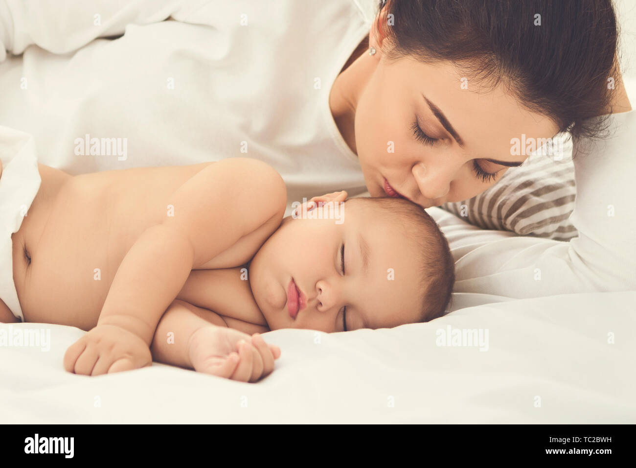 Mother kissing her sleeping newborn baby in bed Banque D'Images