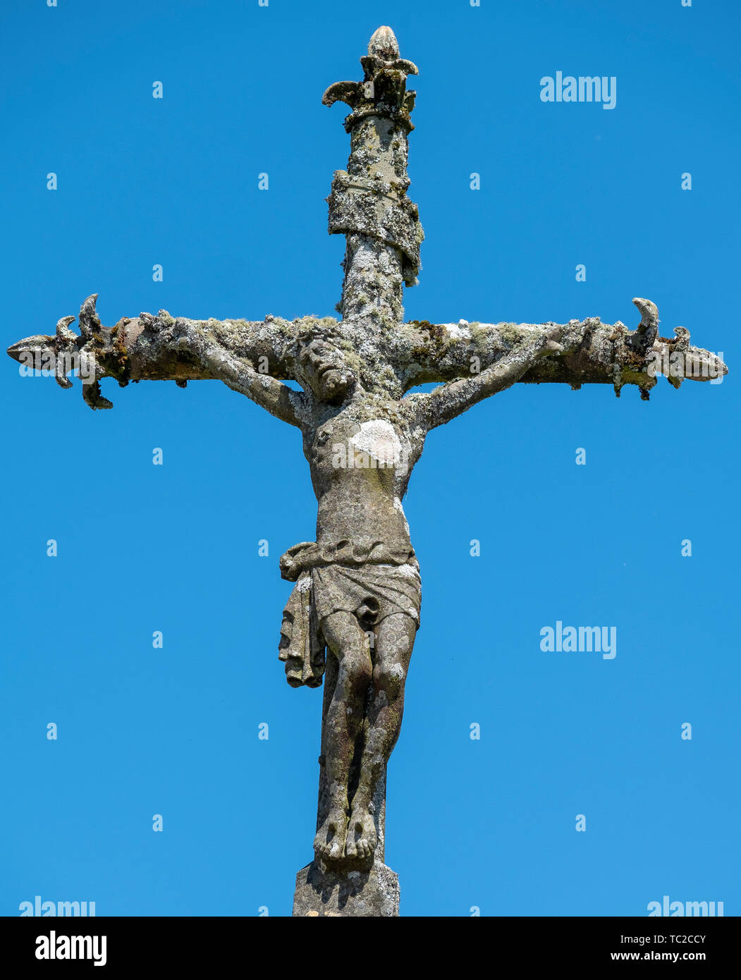 Statue de pierre du Christ sur la croix contre un ciel bleu à un cimetière de la Feuillée, Bretagne, France. Banque D'Images