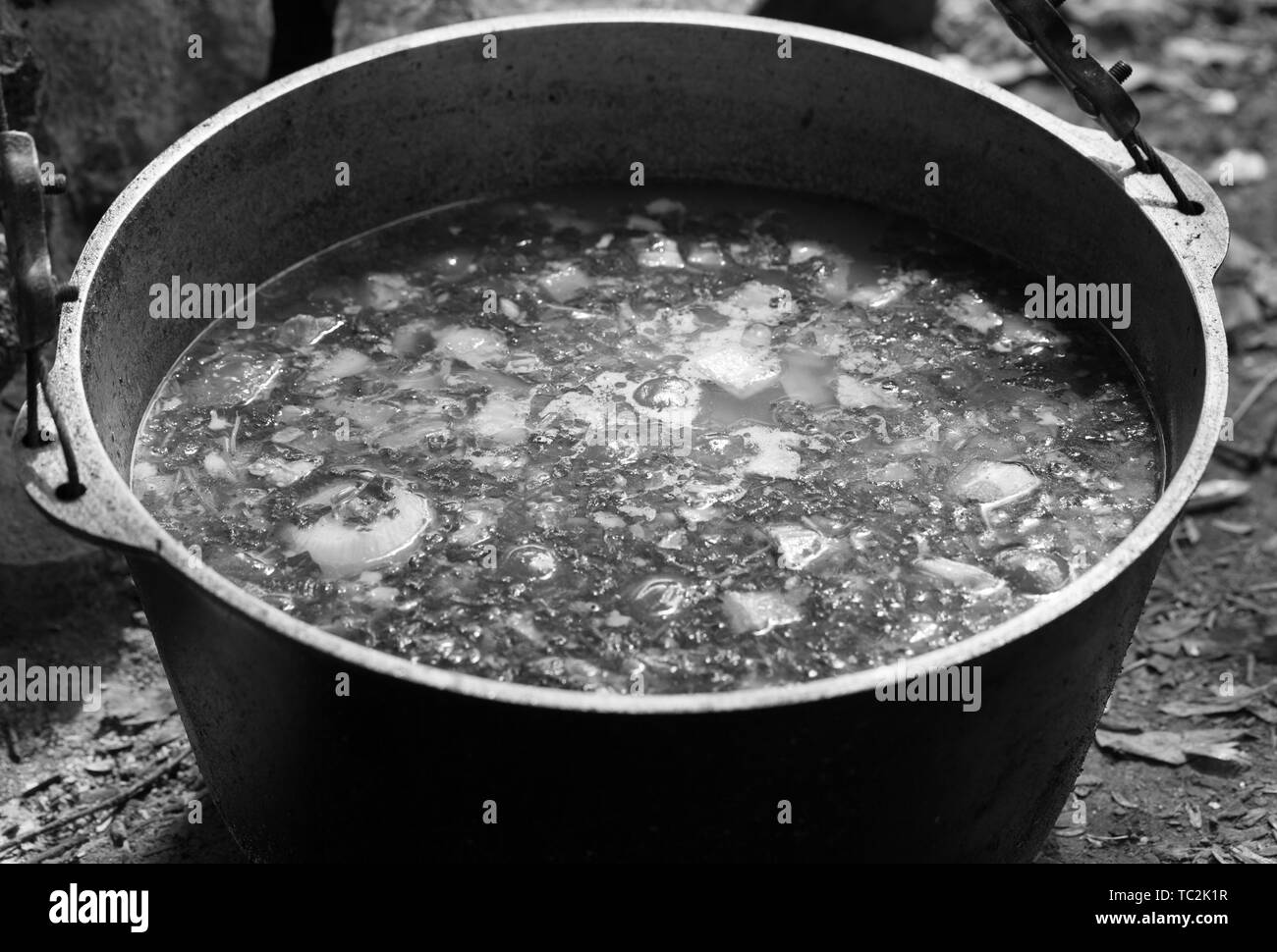Soupe chaude fraîchement préparé dans le chaudron de suie feu de camp. Camping en plein air de la cuisson. Image aux tons noir et blanc. Banque D'Images