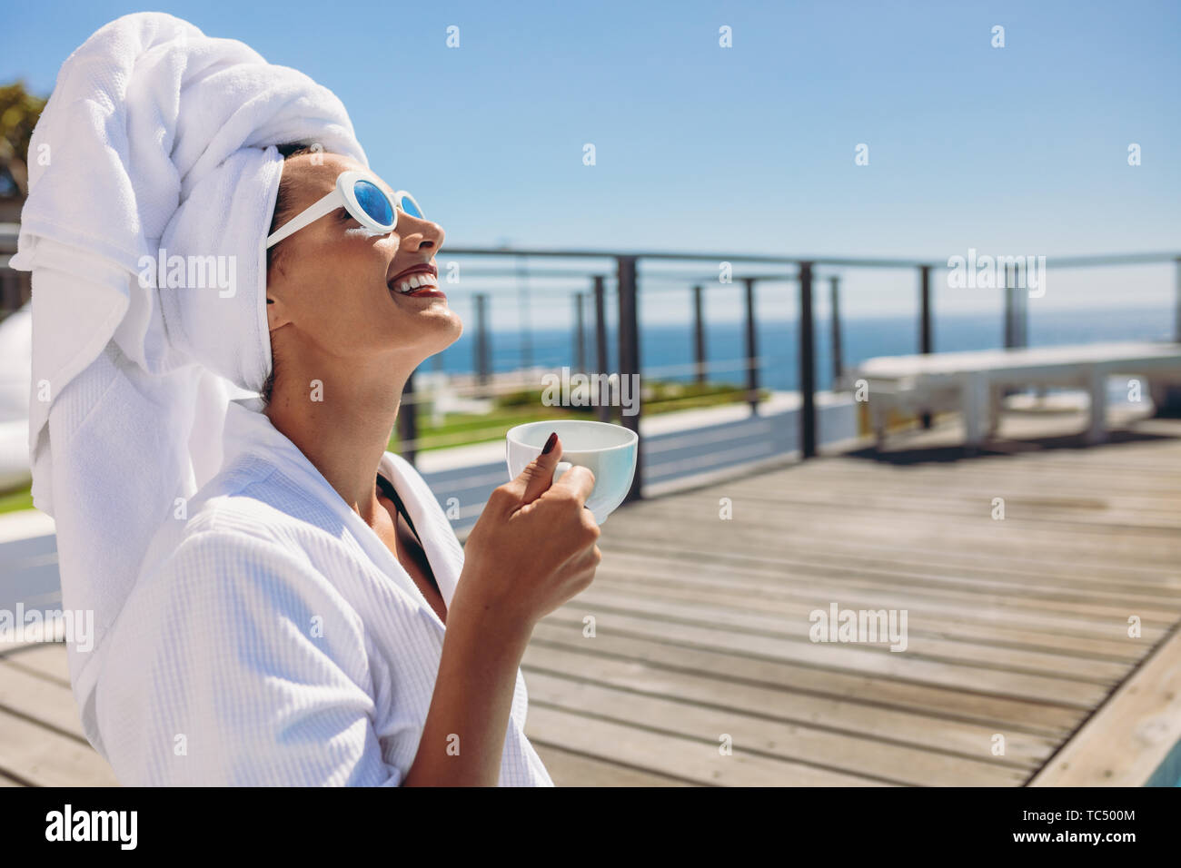 Cheerful woman en peignoir au bord de l'eau avec une tasse de café. Smiling caucasian female having coffee après une baignade. Banque D'Images