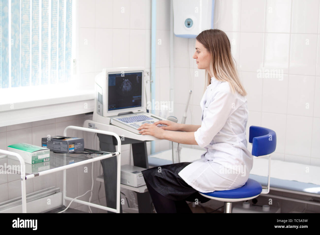 Blonde femme médecin en uniforme blanc dans l'hôpital clinique fonctionne sur échographe. Diagnostic, l'échographie et la notion de santé. copyspase Banque D'Images