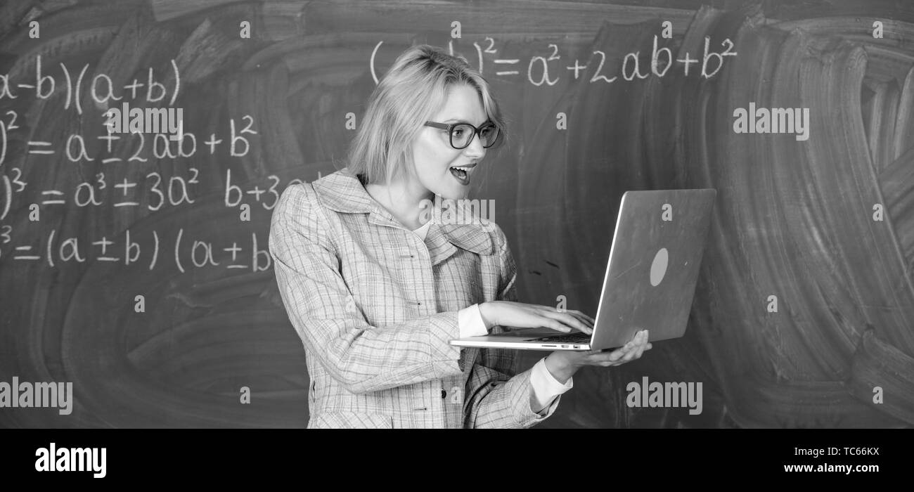 Dame intelligente smart éducateur avec ordinateur portable moderne recherche d'informations d'arrière-plan du tableau. L'apprendre de manière simple. Scolarité en ligne concept. Enseignante portent des lunettes est titulaire d'ordinateur portable Internet surf. Banque D'Images