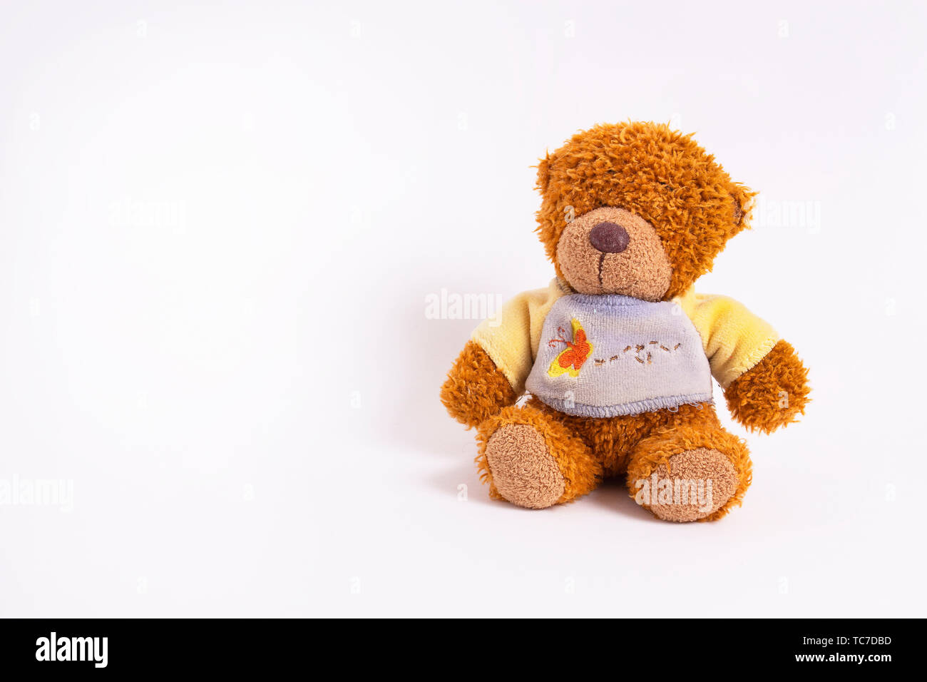 Un petit ours en peluche dans un pull bleu-jaune se trouve sur un fond blanc. Peluche de l'enfant. Enfance heureuse Banque D'Images