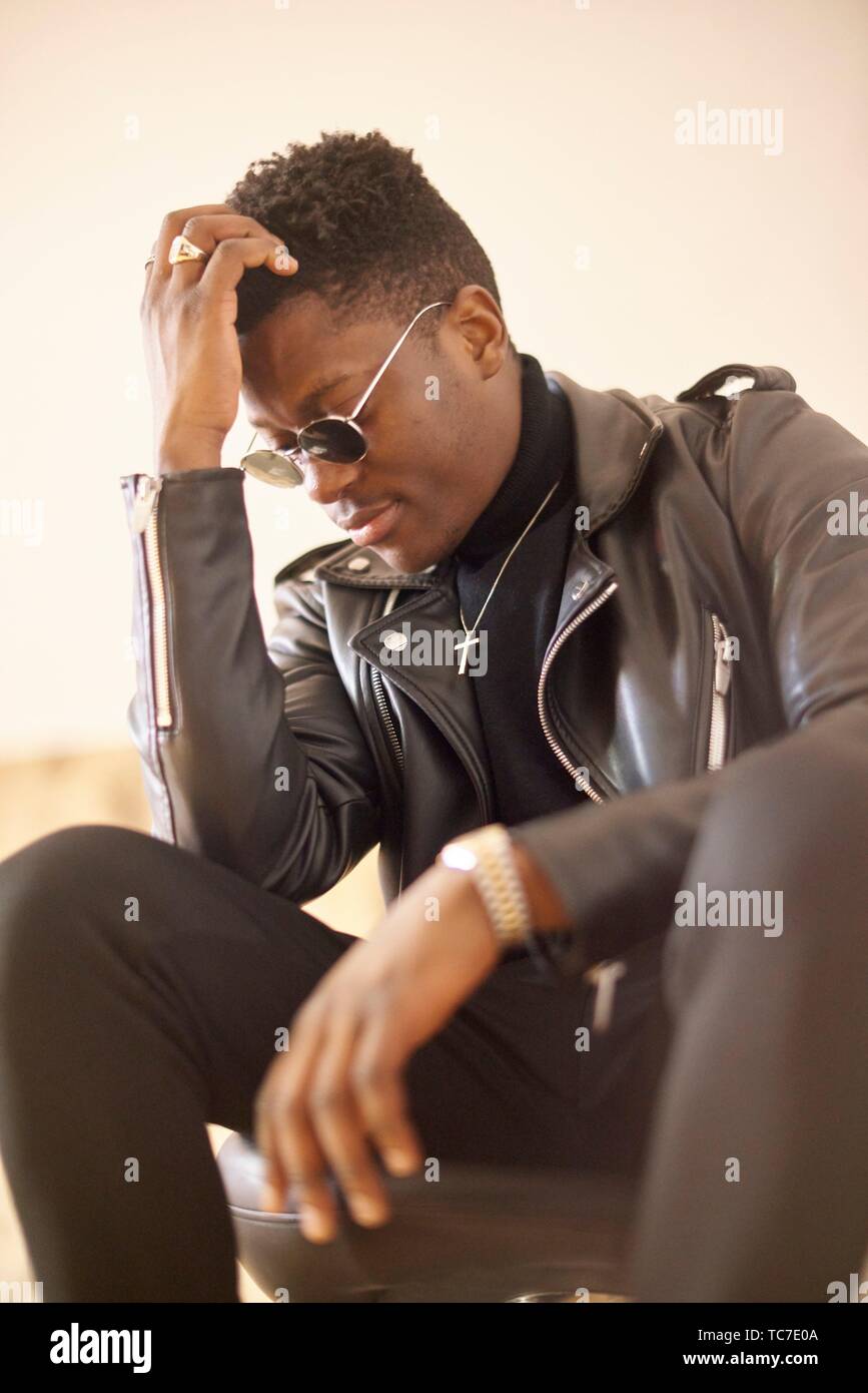 Portrait of young African man leaning head en main, le port de lunettes de soleil et collier croix chrétienne à l'intérieur de Munich, en Allemagne. Banque D'Images