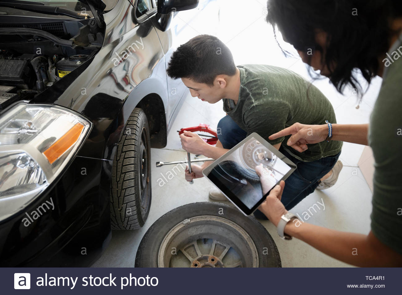 La mère et le fils avec tablette numérique apprendre à changer un pneu de voiture Banque D'Images