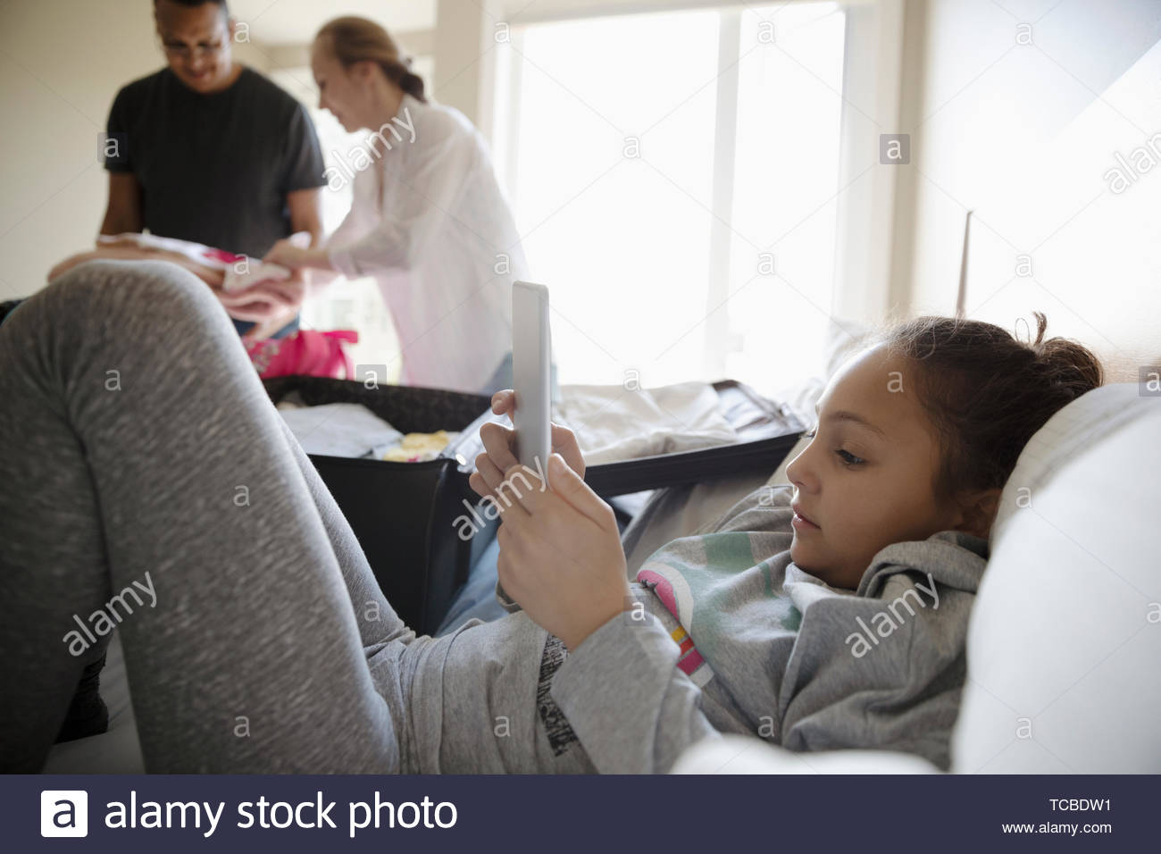 Girl sitting on bed tandis que les parents pack valises pour les locations Banque D'Images