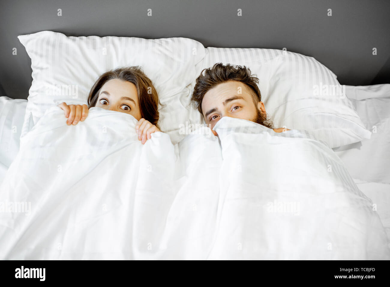 Jeune couple peur de se cacher sous les draps à la maison Photo Stock -  Alamy