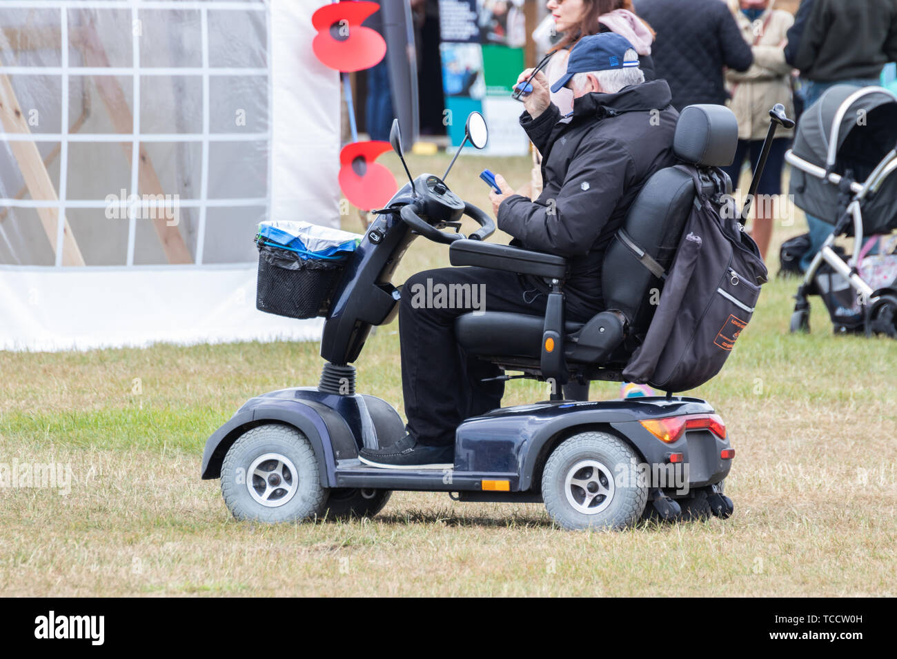 Un homme d'âge moyen sur un scooter de mobilité en utilisant son téléphone mobile ou téléphone cellulaire Banque D'Images