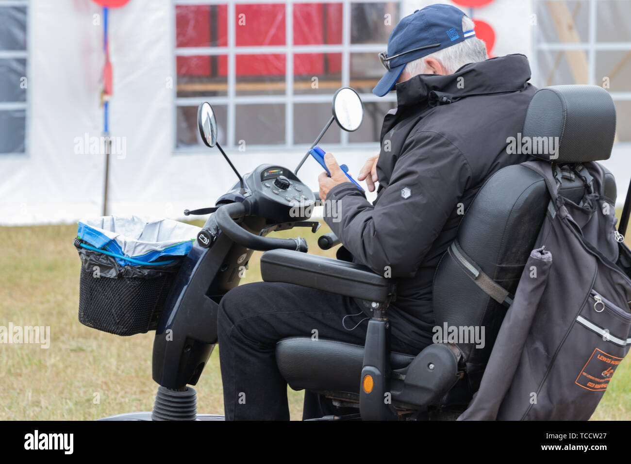 Un homme d'âge moyen sur un scooter de mobilité en utilisant son téléphone mobile ou téléphone cellulaire Banque D'Images