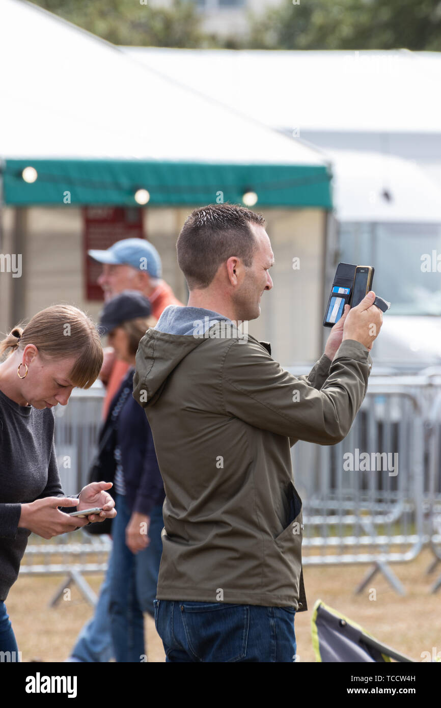 Un homme à l'aide d'un téléphone mobile ou un téléphone cellulaire pour prendre une photo à un événement en plein air Banque D'Images