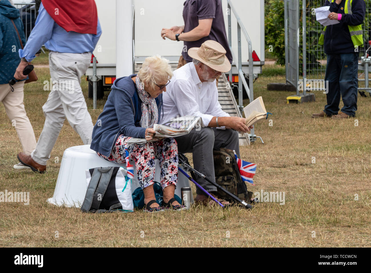 L'âge de la retraite d'un couple assis sur un banc de la lecture pendant un concert en plein air l'un de lire un livre et d'un lit le journal Banque D'Images