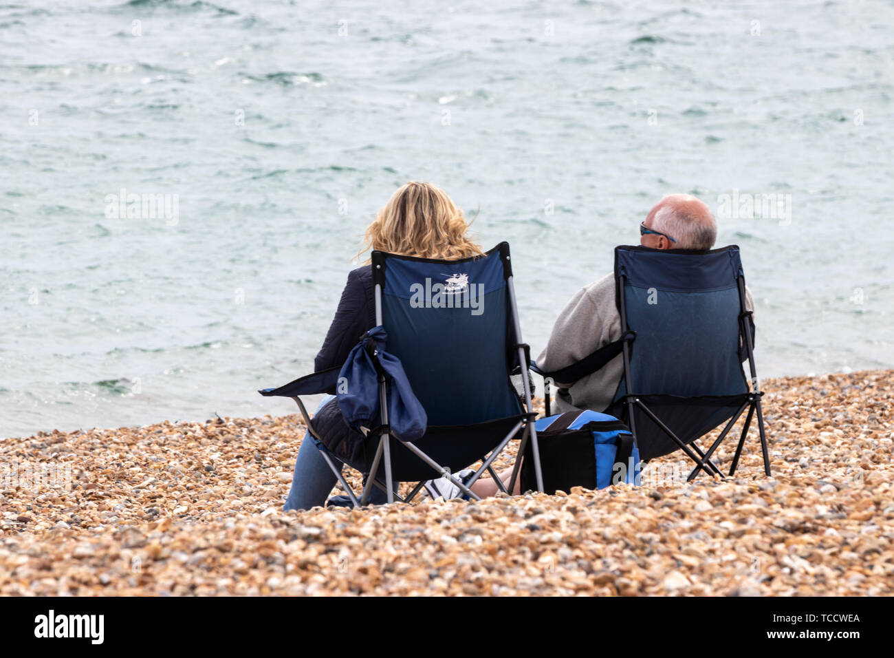 Un couple d'âge moyen s'assit sur les chaises ou chaises de camping sur une plage de galets de la mer Banque D'Images