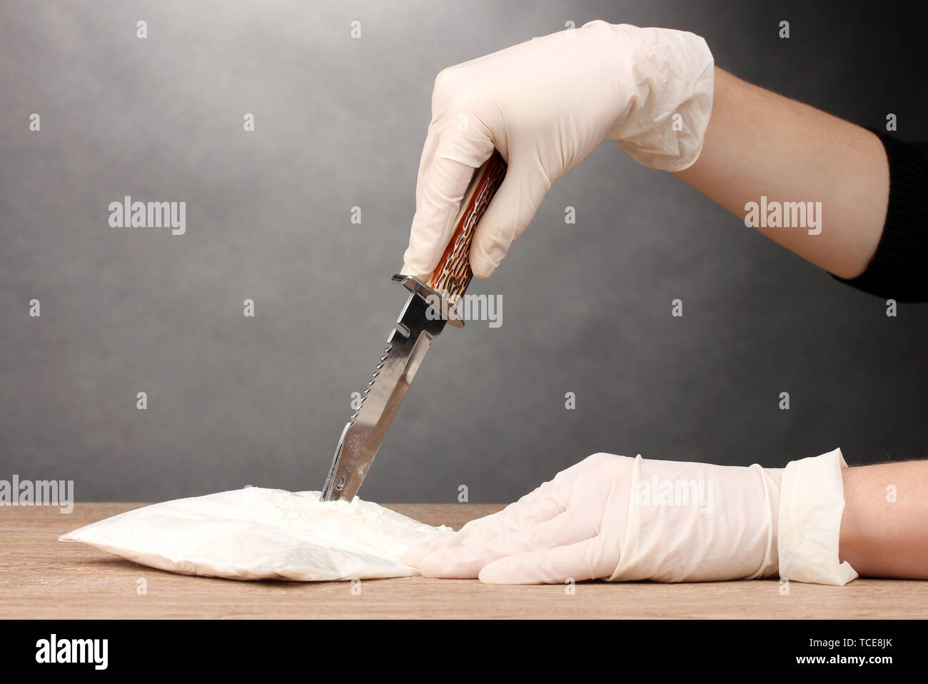 L'ouverture des paquets de cocaïne à l'aide d'un couteau sur la table en bois sur fond gris Banque D'Images