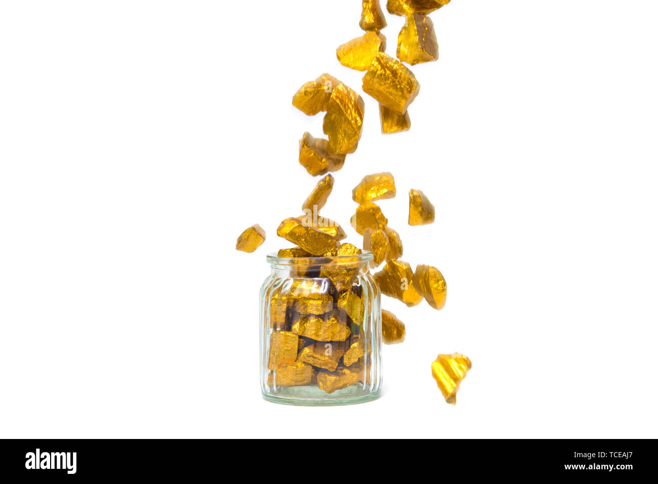 La chute des pépites d'or, le minerai d'or , pierre précieuse ou forfaitaire en pierres dorées et bocal verre isolé sur fond blanc. Banque D'Images