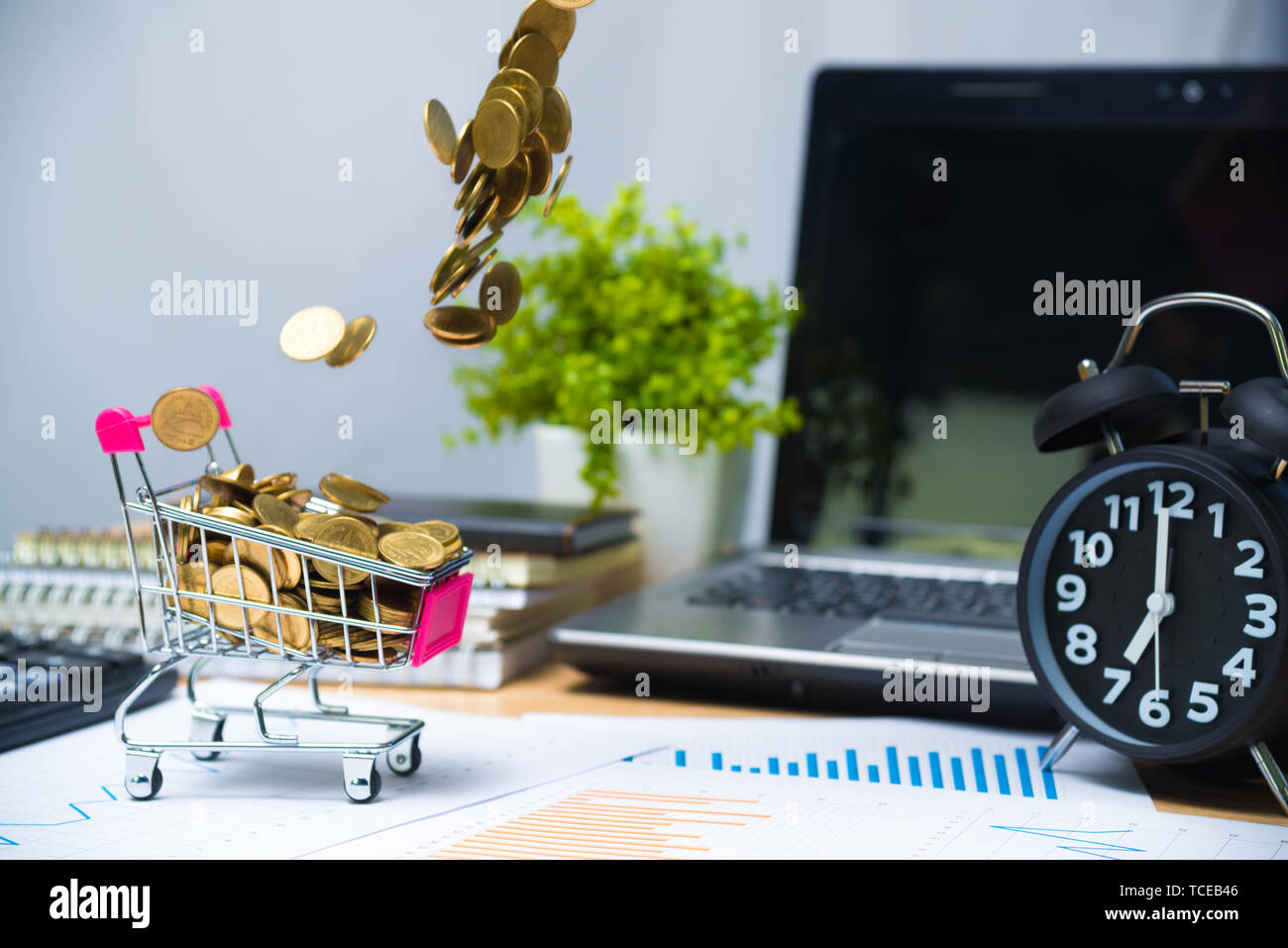 Tomber des pièces d'or dans votre panier Chariot de supermarché ou sur la table de travail avec des fournitures de bureau ou du travail de bureau outils essentiels pour l'entreprise articles fin Banque D'Images