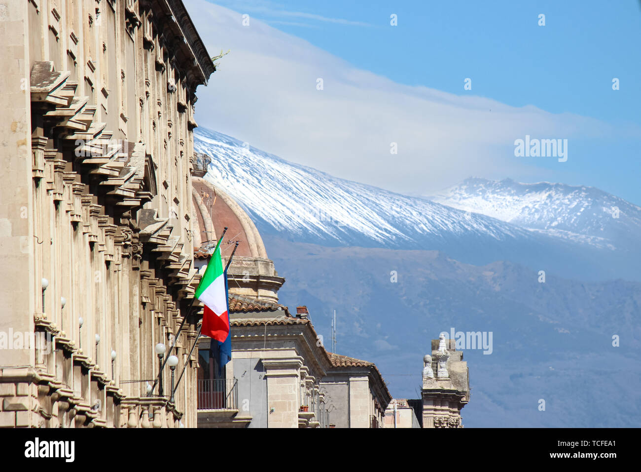 Bâtiment historique de Catane, Sicile, Italie avec agitant drapeau italien. Dans l'arrière-plan coupole de Sainte Agathe célèbre cathédrale et de l'Etna avec de la neige sur le sommet du volcan. Banque D'Images