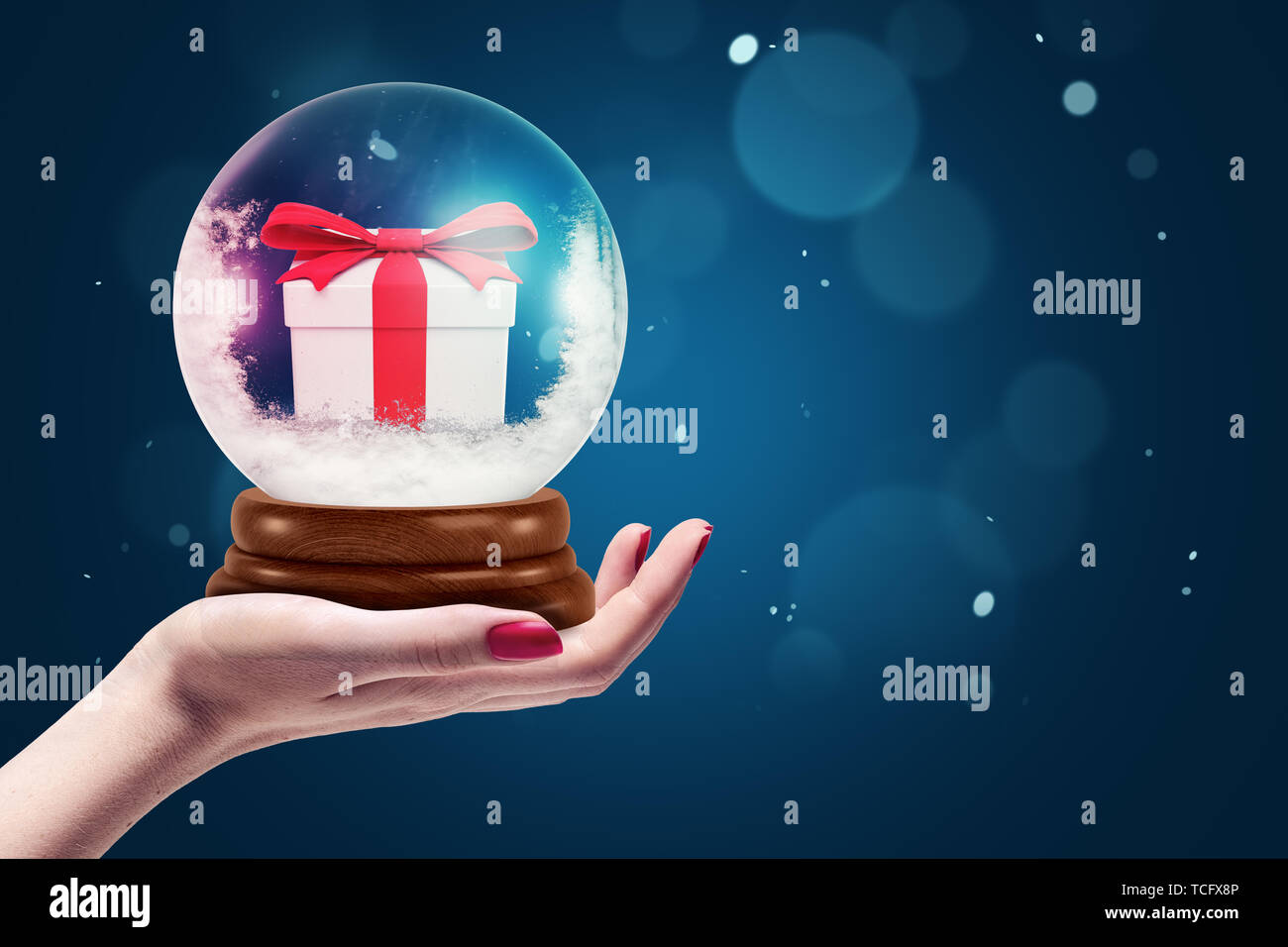 Closeup of woman's hand holding boule de cristal de neige et petit cadeau fort à l'intérieur sur fond bleu avec copie espace. Banque D'Images