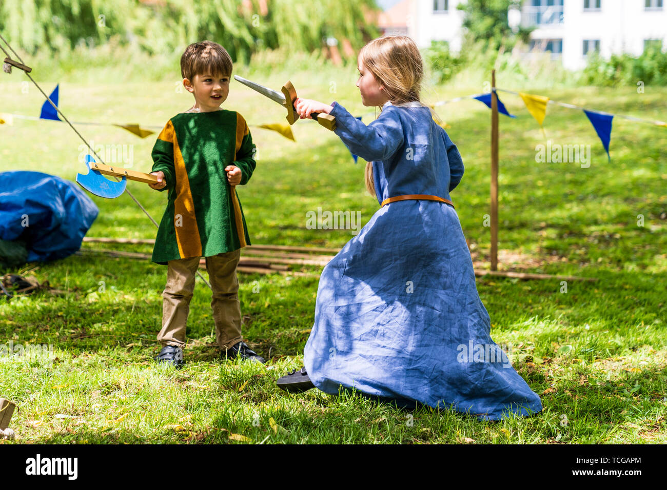 Le week-end médiéval. Portrait de deux jeunes enfants, garçon, 4-5 ans, et une fille, 5-6 ans, vêtu de vêtements médiévaux et des combats à l'épée et espièglerie ax dans l'herbe avec saule derrière. Banque D'Images