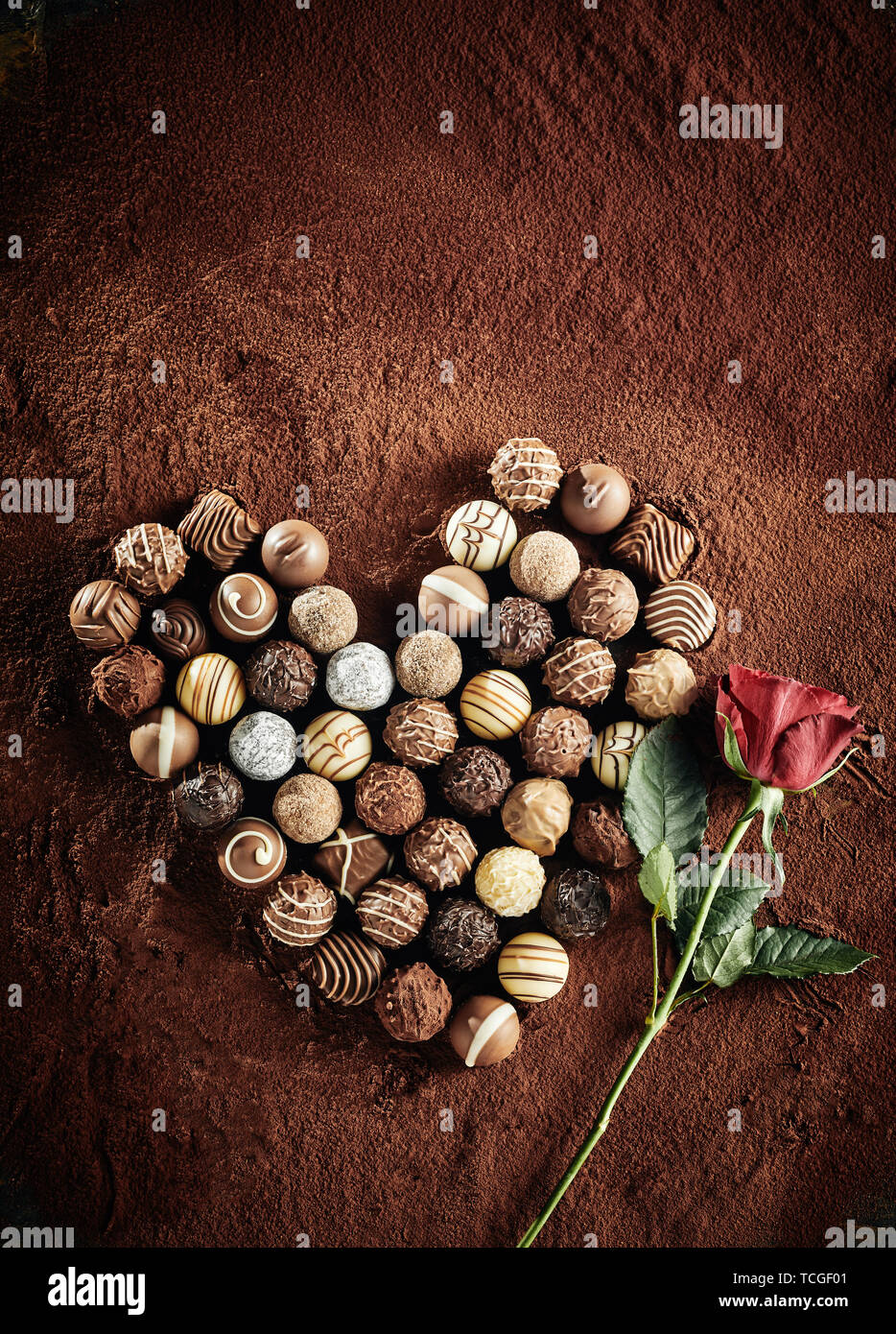 Encore en forme de coeur d'une vie de luxe sélection assorties bonbons de chocolat noir sur un lit de poudre de cacao avec une rose rouge symbolique de l'amour annonce romance avec co Banque D'Images