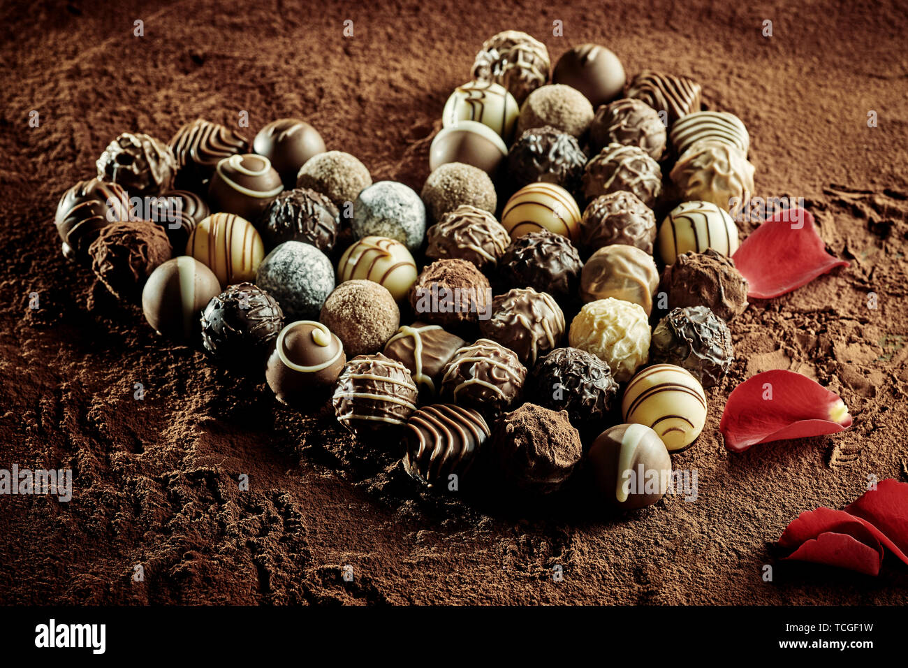 Pétales de rose rouge à côté d'un assortiment de délicieux petits bonbons de chocolat noir rond placé dans la forme de coeur Banque D'Images