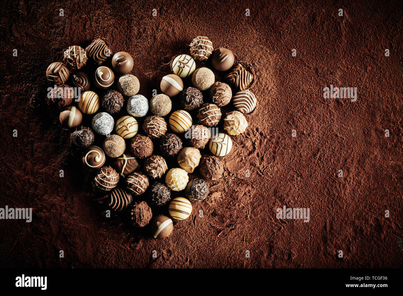 Chocolat artisanal de luxe les pralines dans un cœur symbolique de romance et d'amour sur fond de cacao poudre avec copie espace pour la St Valentin Banque D'Images