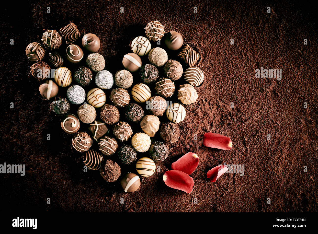 Vue de dessus de la sphère gastronomique pose de chocolat en forme de coeur pour symboliser l'amour à côté de pétales de rose Banque D'Images