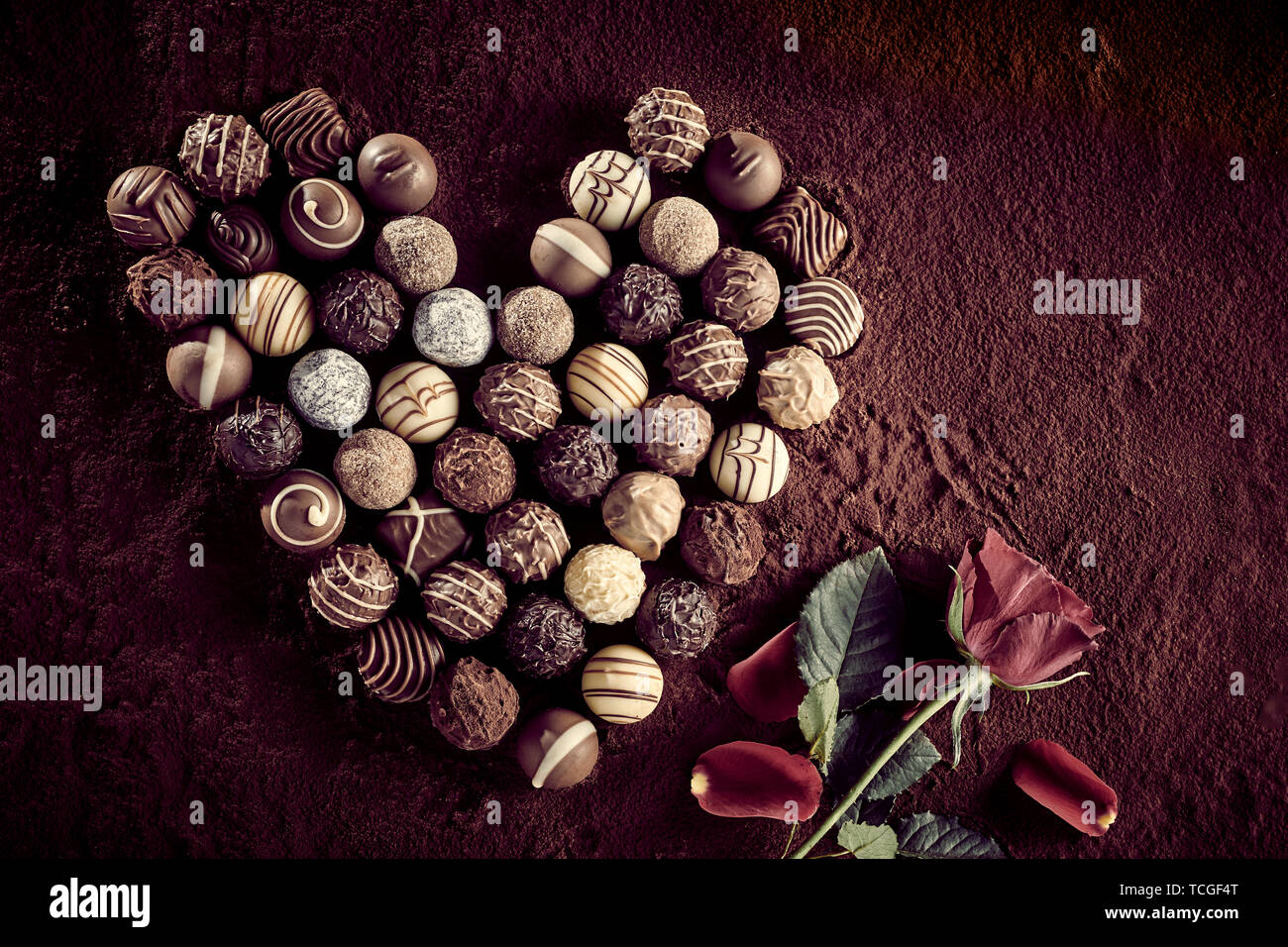 Vue supérieure de l'assortiment de nombreux petits chocolats décorés gastronomique à côté de rose rouge sur fond brun Banque D'Images