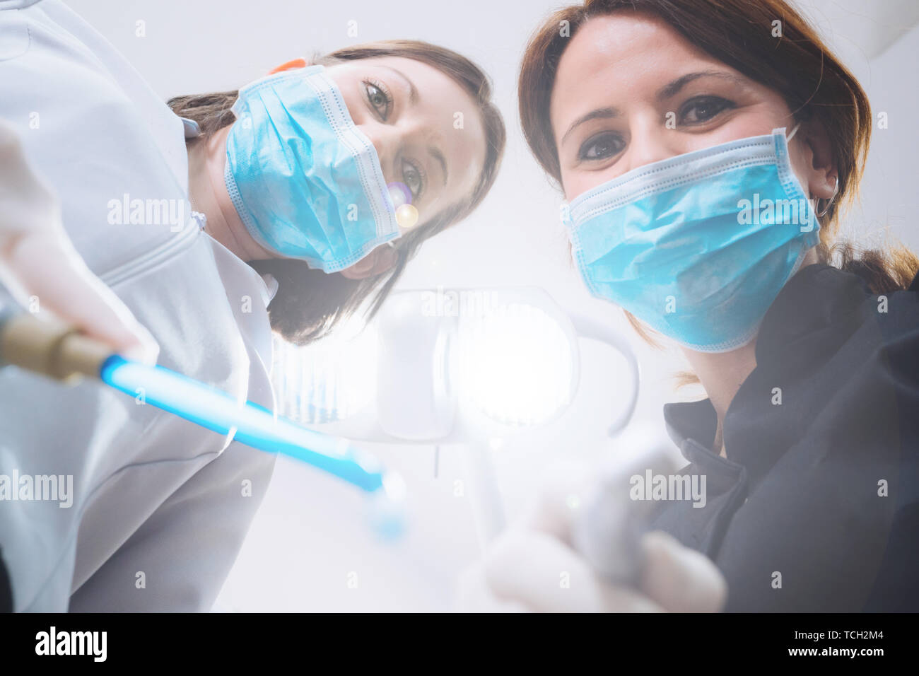 Vue de dessous de deux femmes dentistes dans le masque chirurgical et outils de maintien à l'appareil photo à. Point de vue du patient au dentiste. Banque D'Images