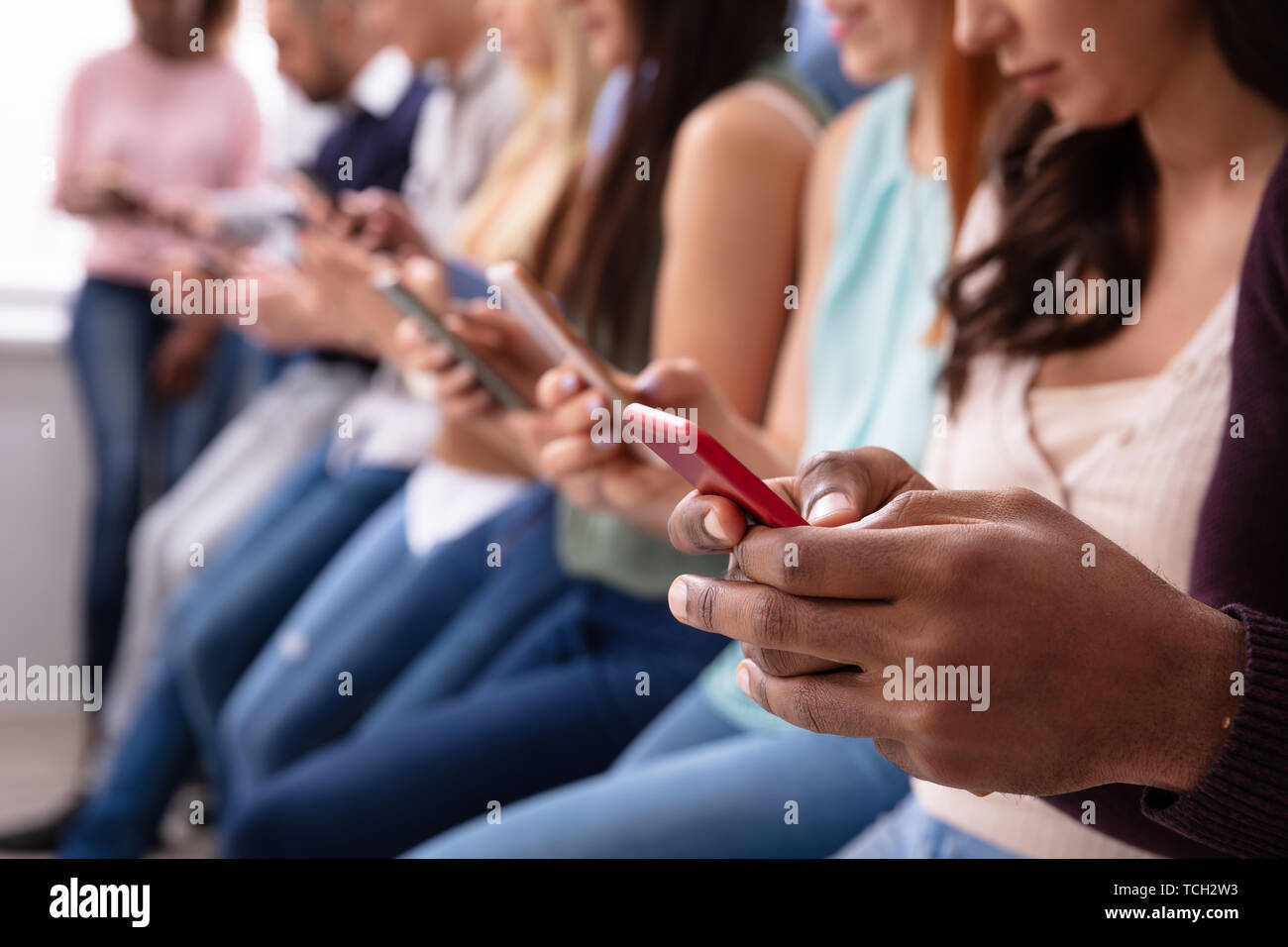 Les jeunes multi-ethnique se penchant près de table en ligne à l'aide de téléphone intelligent Banque D'Images