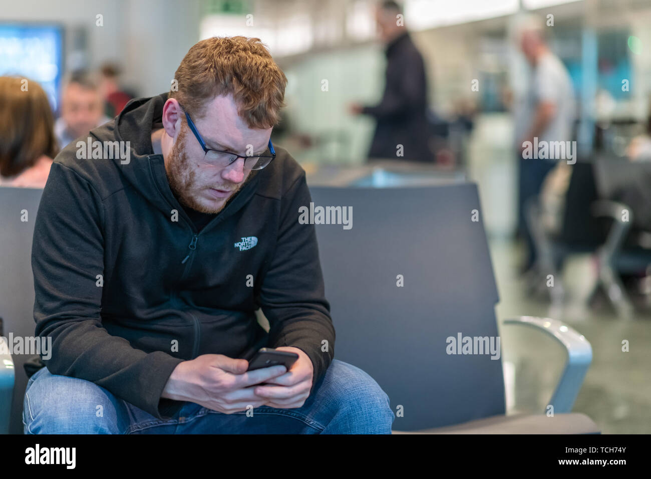 Un homme est assis dans un aéroport terminal départ texting ses proches en attente de son prochain vol retour à l'accueil Banque D'Images