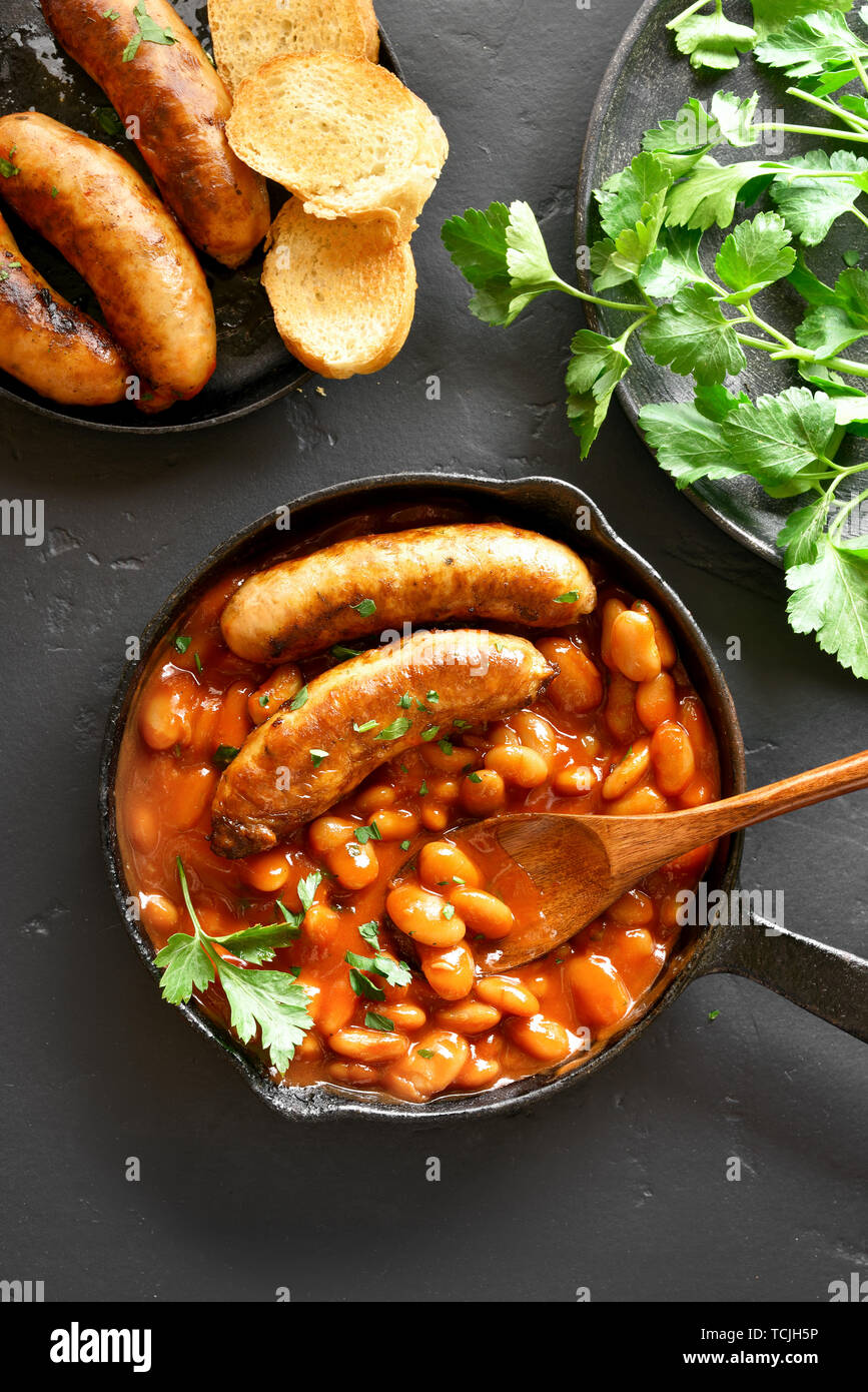 Saucisses grillées avec des haricots blancs à la sauce tomate dans la poêle à fond en pierre noire. Haut de la vue, télévision lay Banque D'Images