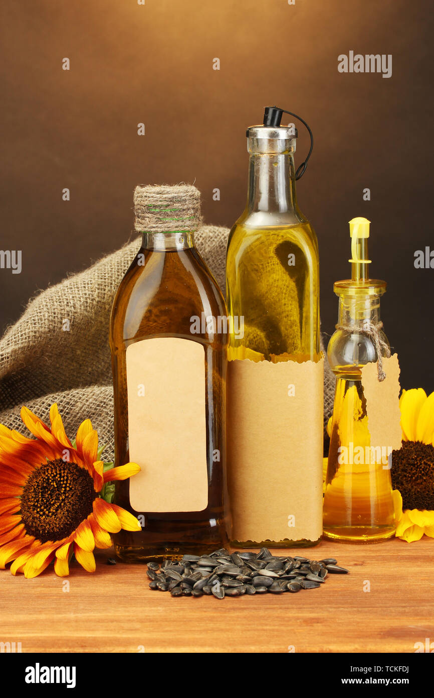 En bouteilles d'huile, de tournesol et de graines, sur table en bois sur fond brun Banque D'Images