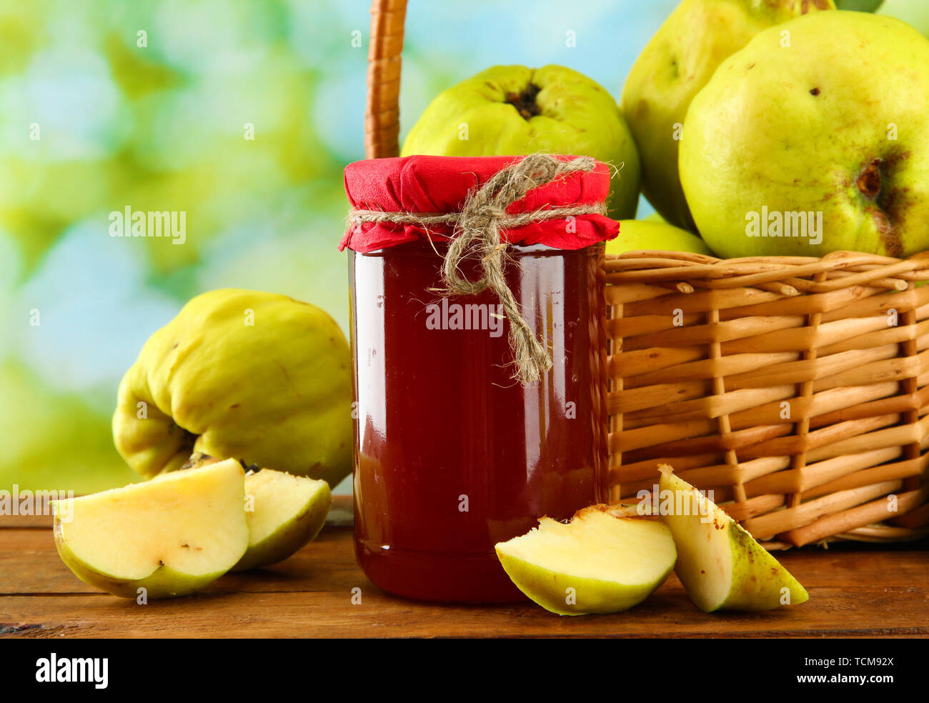 Pot de confiture et coings avec des feuilles dans le panier, sur fond vert Banque D'Images