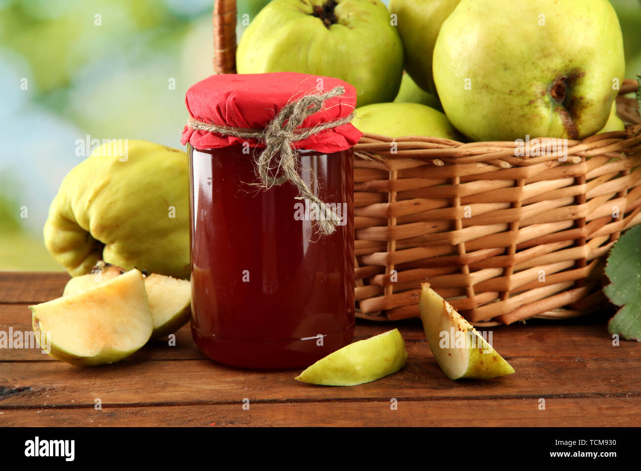 Pot de confiture et coings avec des feuilles dans le panier, sur fond vert Banque D'Images