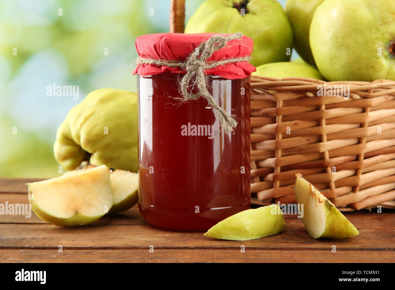 Pot de confiture et coings avec des feuilles dans le panier, sur fond vert Banque D'Images