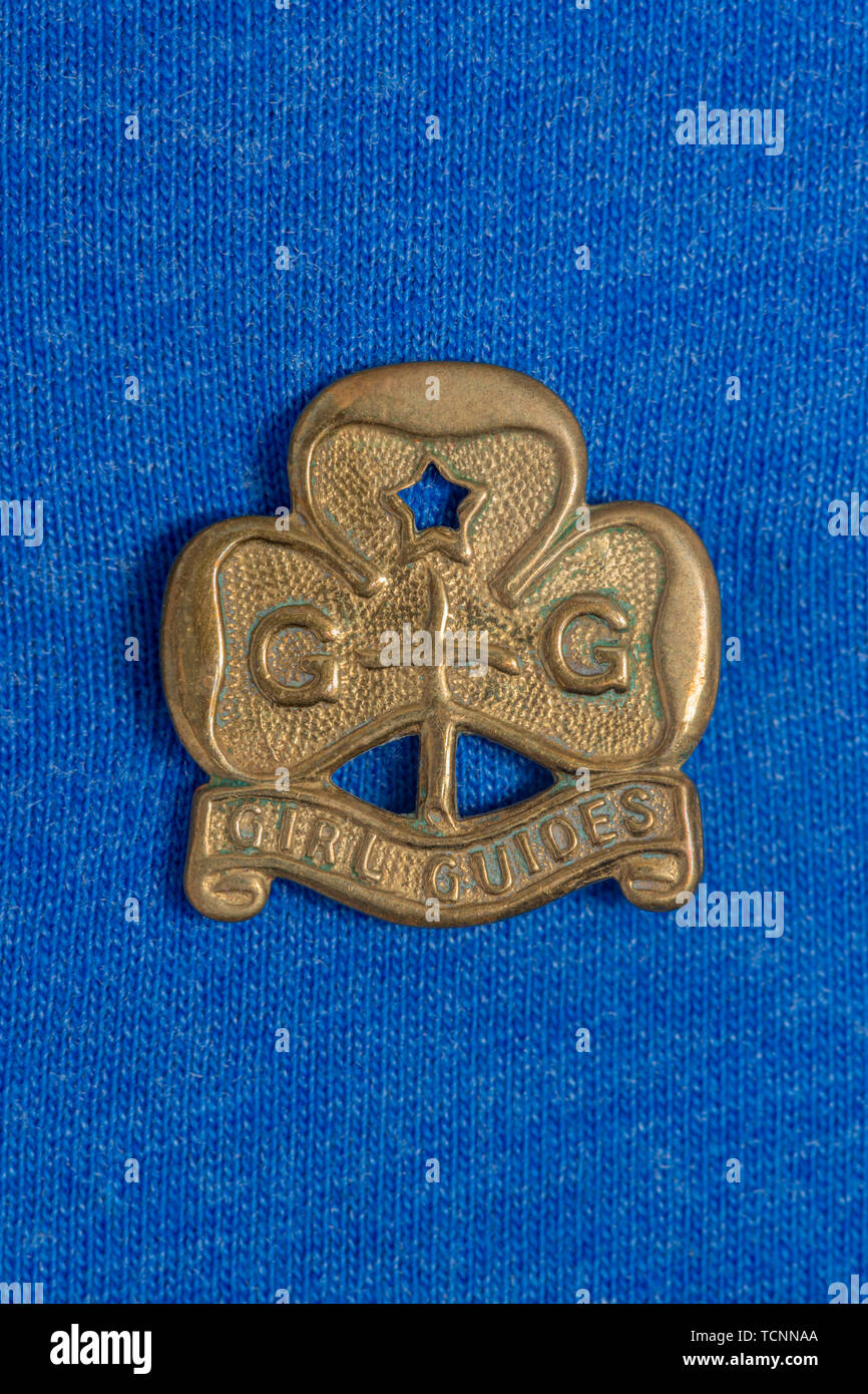 Un laiton vintage Girl Guides d'un insigne tourné sur un fond en coton bleu. Banque D'Images