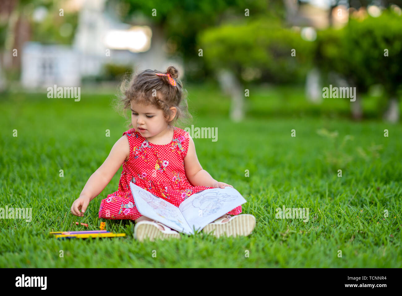 Petite fille d'apprentissage ou d'un dessin à colorier peindre sur l'herbe verte dans la nature au jardin. Banque D'Images