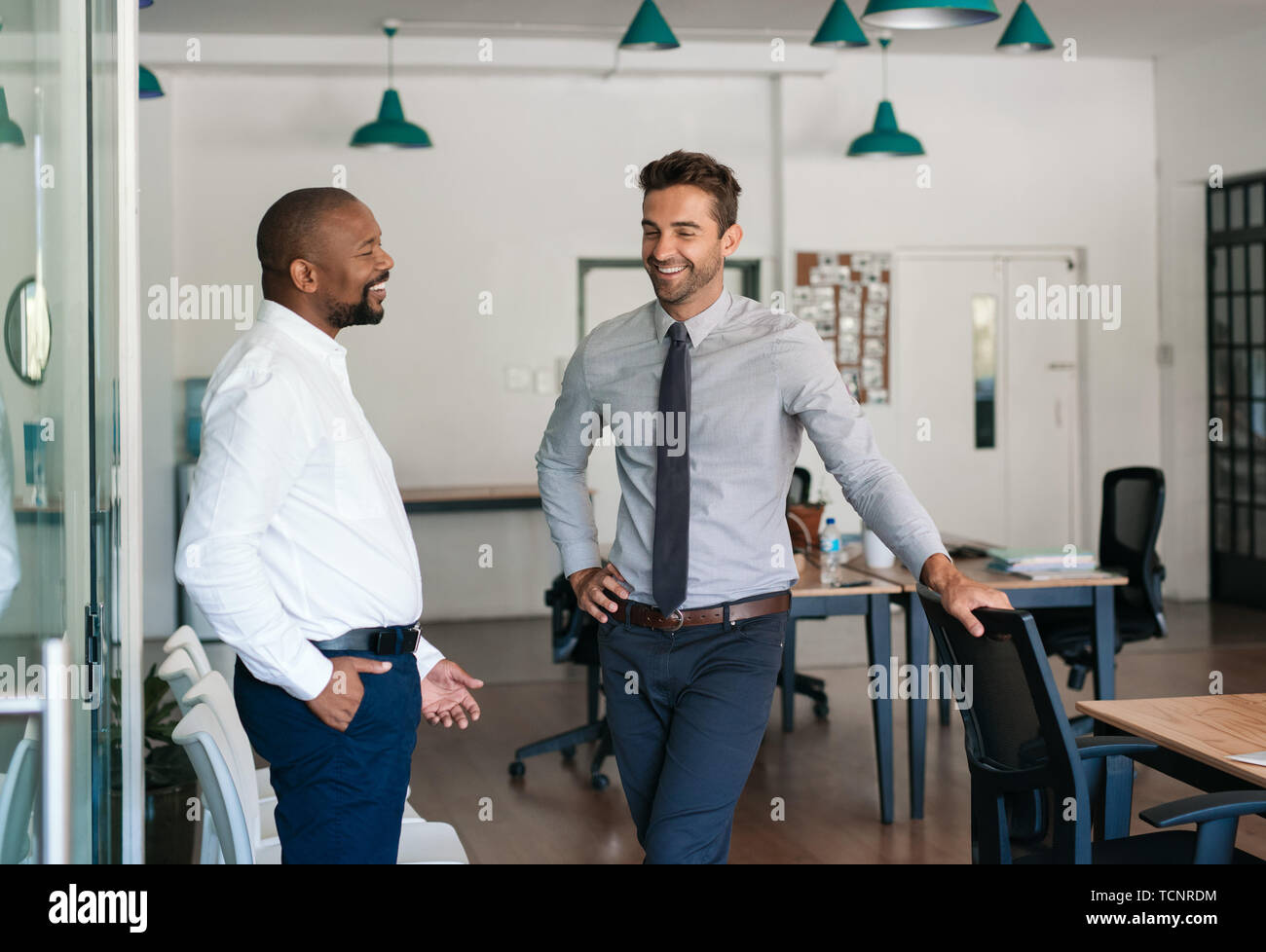 Close up image de deux hommes d'âge mûr parler et rire ensemble tout en se tenant dans un grand bureau moderne Banque D'Images