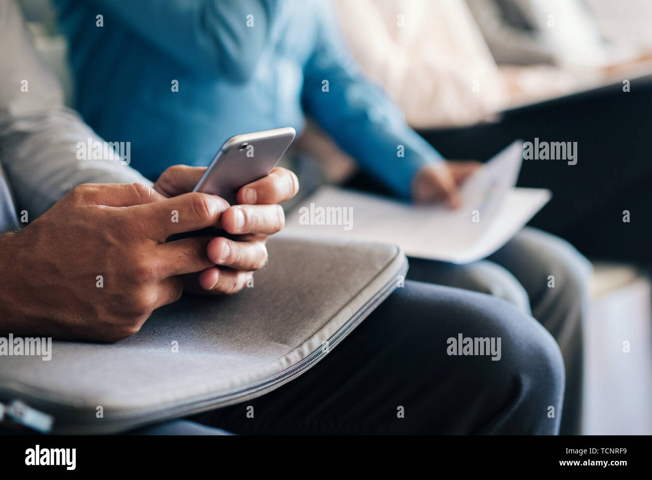 Closeup of hands texting message avec arrière-plan de candidats assis dans des chaises dans un bureau à attendre leur interview Banque D'Images