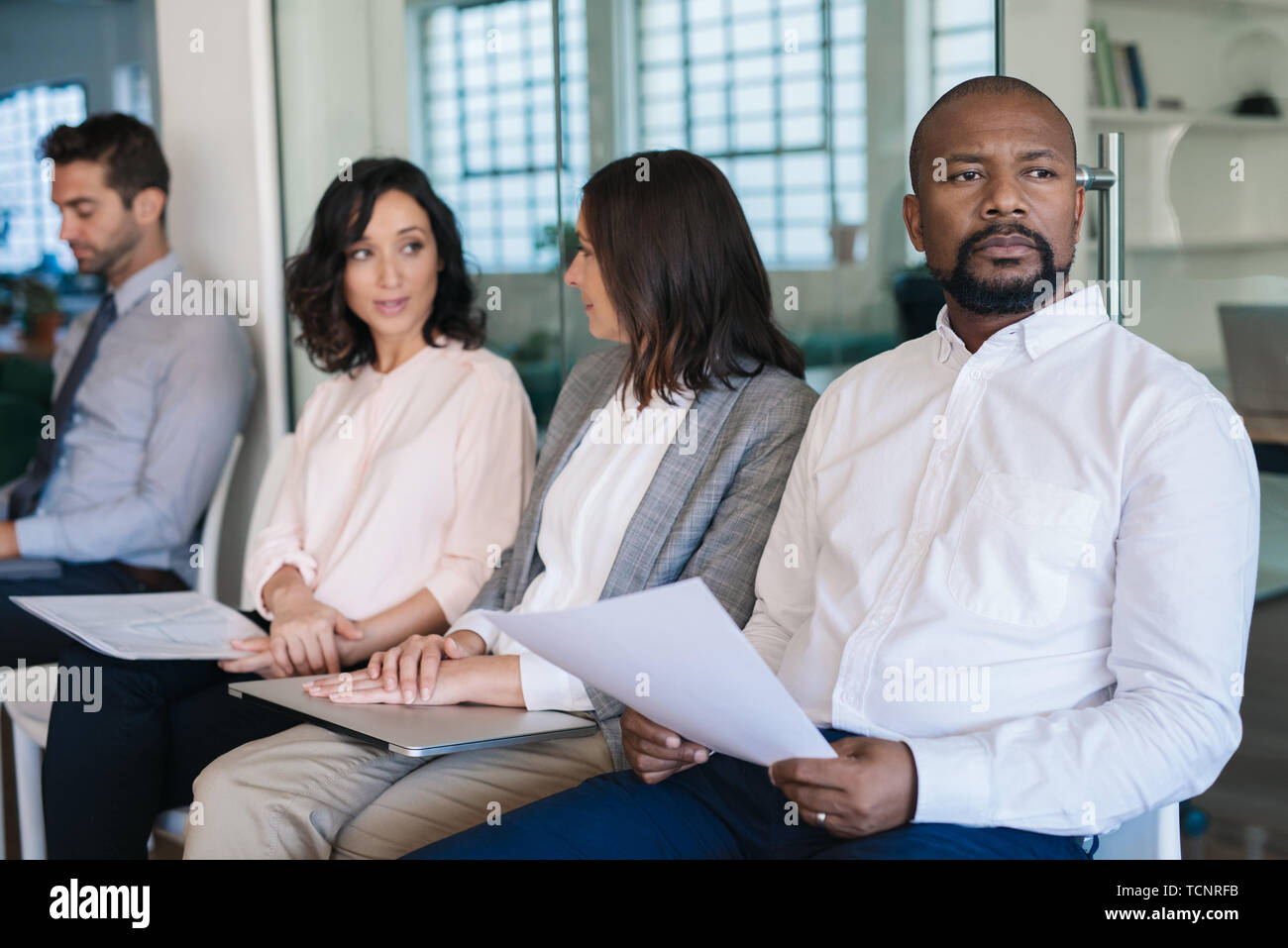 African American demandeur d'emploi tenant son cv et se préparer mentalement pour son entrevue lors d'un entretien avec un groupe d'autres personnes interviewées Banque D'Images