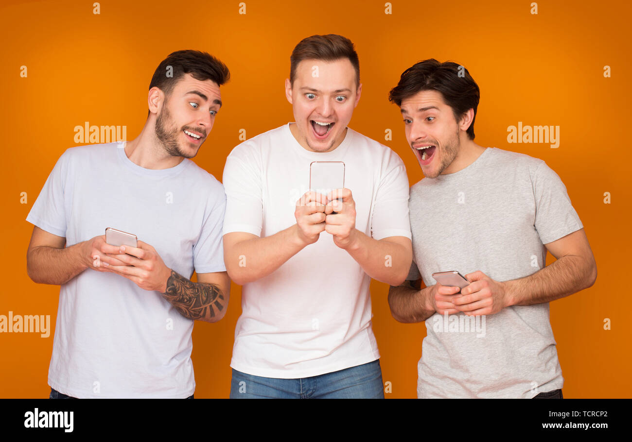 Surpris friends holding les téléphones mobiles, la lecture de bonnes nouvelles Banque D'Images