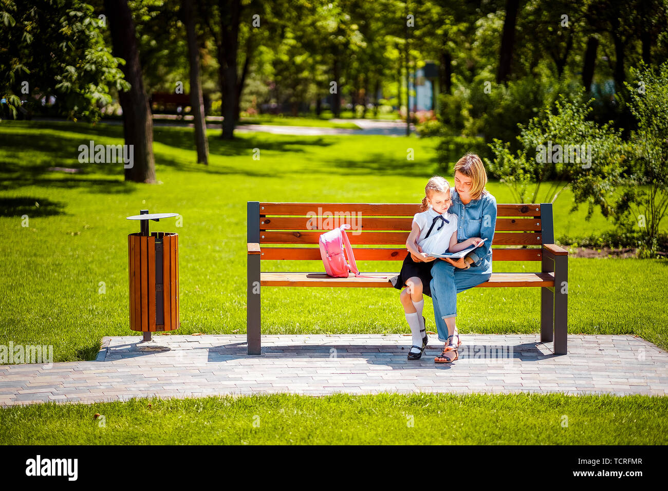 Mère et fille à l'extérieur parc public assis sur le banc et lisez le livre, de l'étude des leçons. Enfant de la parentalité et de concept. Banque D'Images
