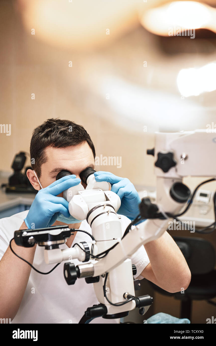 Male dentist portant des uniformes blancs, à la recherche en soins dentaires professionnels microscope binoculaire endodontique avec caméra dans le bureau. Close up Banque D'Images