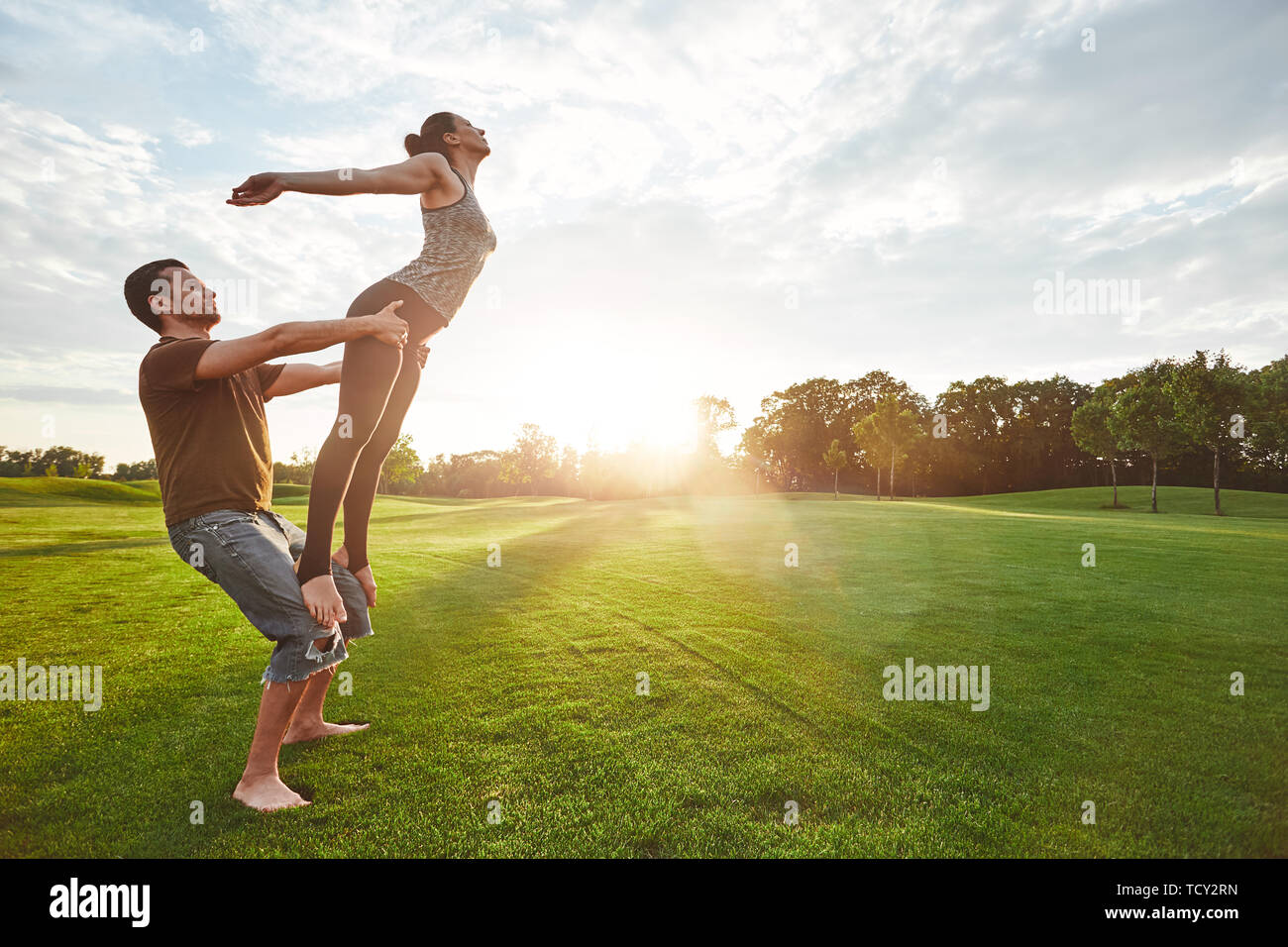 La pratique de l'aviation. Deux personnes pratiquant le yoga acro dans la nature sur un matin ensoleillé. Strong man holding et l'équilibrage femme sur ses genoux. Lifesty sain Banque D'Images