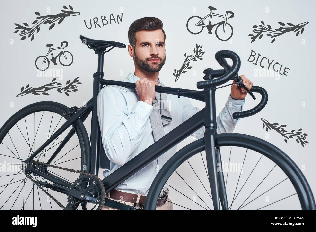 Best transport. La photo en gros du bon à l'homme dans les tenues de transporter son vélo en position debout contre l'arrière-plan gris avec la main doodl Banque D'Images