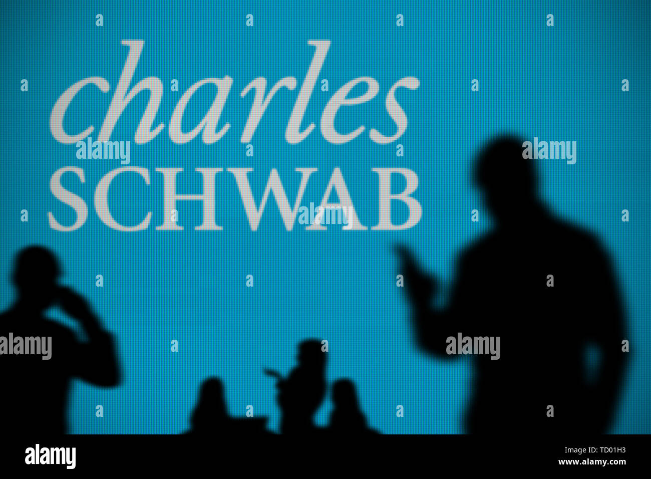 Le logo Charles Schwab est vu sur un écran LED à l'arrière-plan tandis qu'une personne utilise la silhouette d'un smartphone dans l'avant-plan (usage éditorial uniquement) Banque D'Images