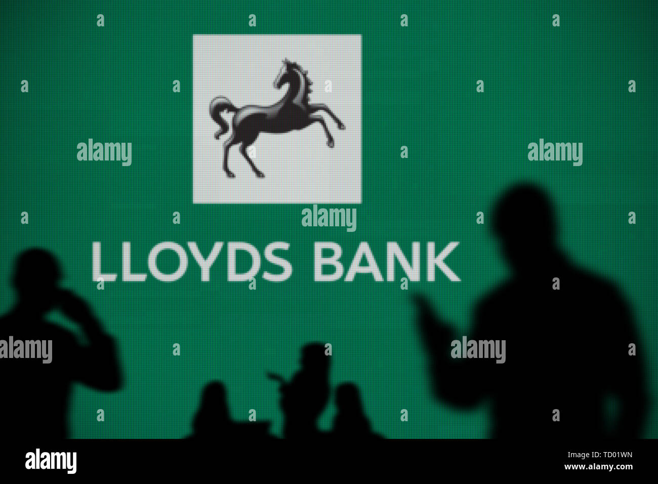 La Banque Lloyds logo est visible sur un écran LED à l'arrière-plan tandis qu'une personne utilise la silhouette d'un smartphone dans l'avant-plan (usage éditorial uniquement) Banque D'Images