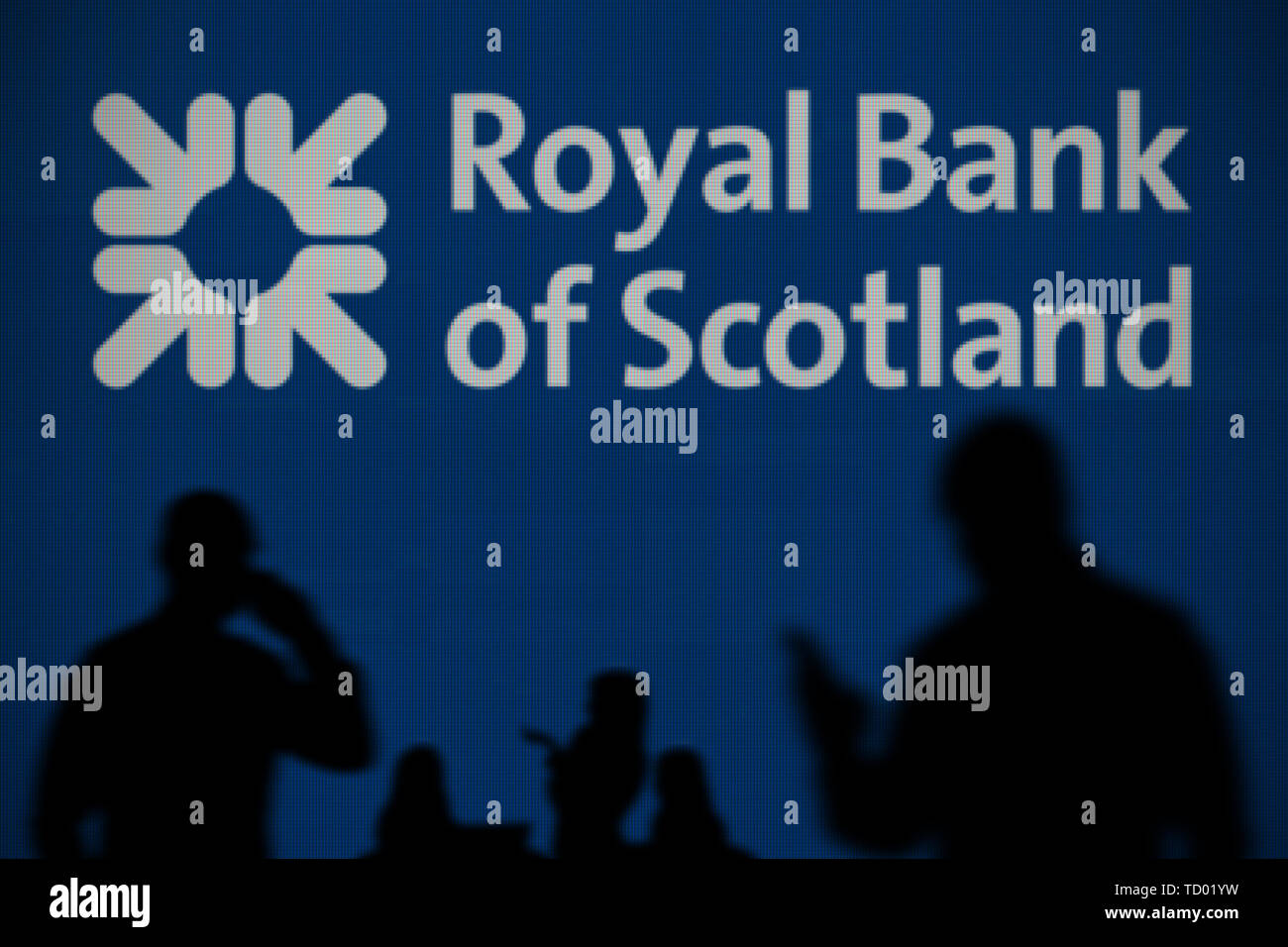 Le logo RBS est vu sur un écran LED à l'arrière-plan tandis qu'une personne utilise la silhouette d'un smartphone dans l'avant-plan (usage éditorial uniquement) Banque D'Images