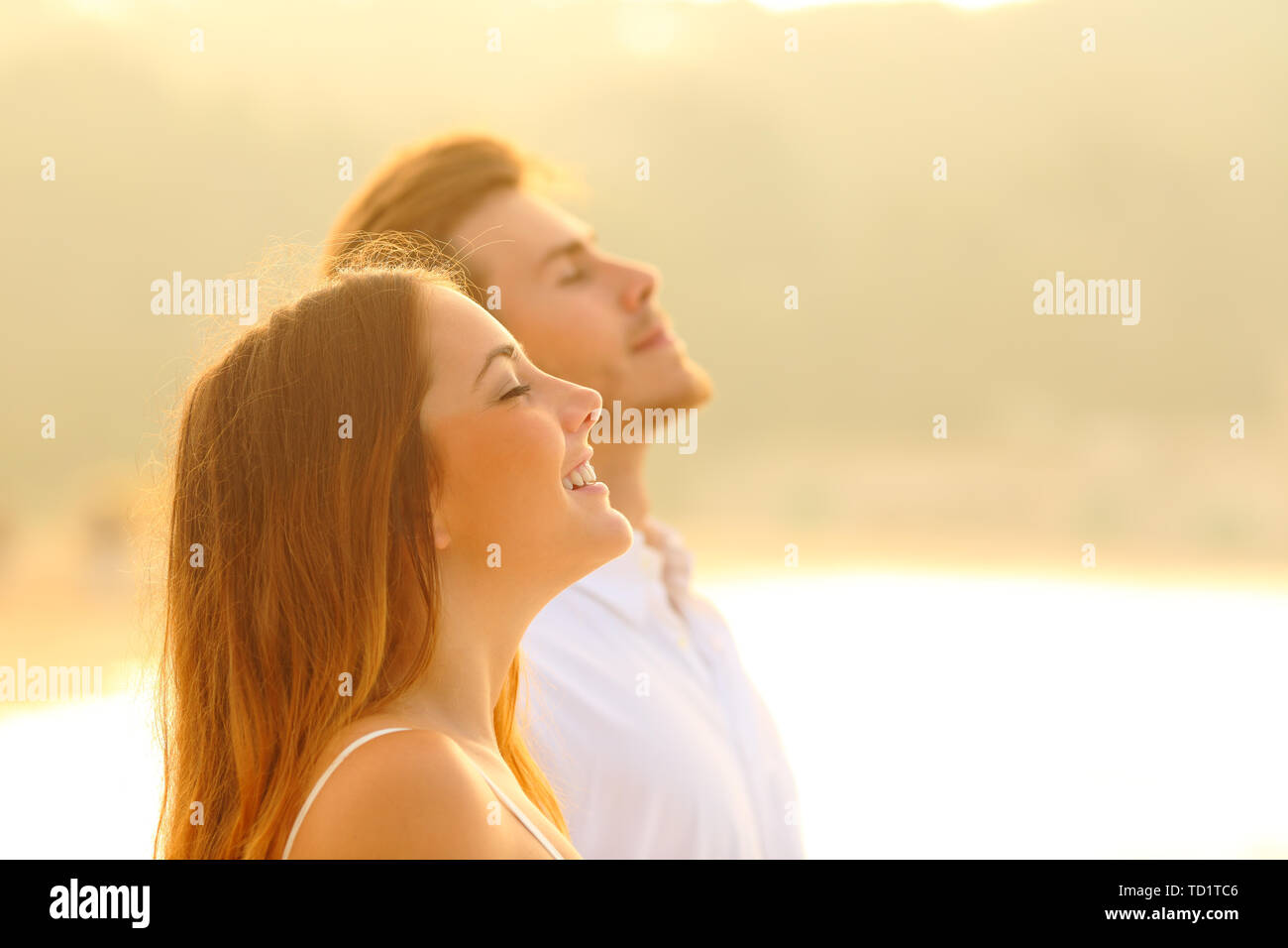 Vue de côté portrait d'un couple heureux sur la plage respirer profondément l'air frais au coucher du soleil Banque D'Images
